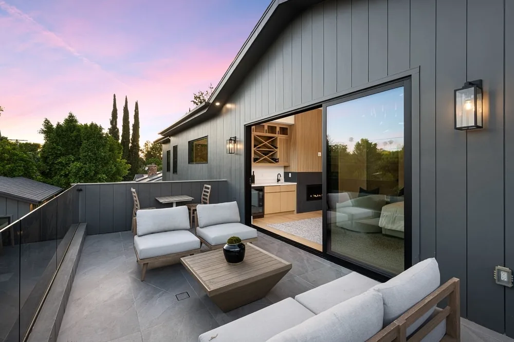 Modern outdoor patio with comfortable seating and a view of the sunset sky, adjacent to a stylish interior living space.
